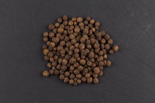 Large black peppercorn seeds on dark stone background