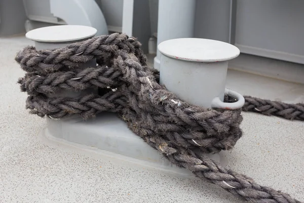 Close-up of a mooring rope with a knotted end tied around a cleat on a wooden pier/ Nautical mooring rope