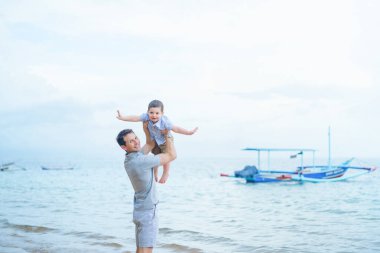 Baba ve küçük çocuk Endonezya 'nın Bali sahilinde kumsalda oynuyorlar.