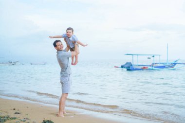 Baba ve küçük çocuk Endonezya 'nın Bali sahilinde kumsalda oynuyorlar.