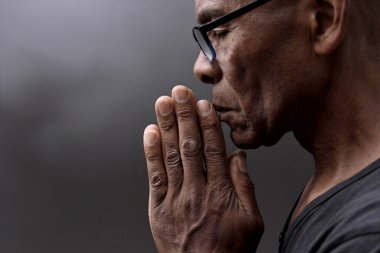 Siyah adam, insanların resimleriyle birlikte gri siyah arka planda Tanrı 'ya dua ediyor.