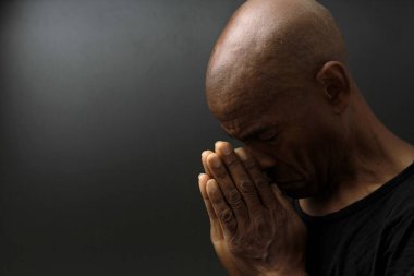 Siyah adam, gri siyah arka planda, insanların fotoğraflarıyla Tanrı 'ya dua ediyor.