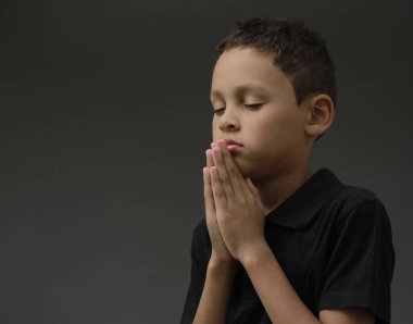 Çocuk Tanrı 'ya dua ediyor, elleri kapalı, gözleri kapalı, gri arka plan fotoğrafında.