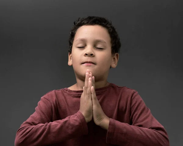 boy praying to God with hands held together with closed eyes on grey background stock photo