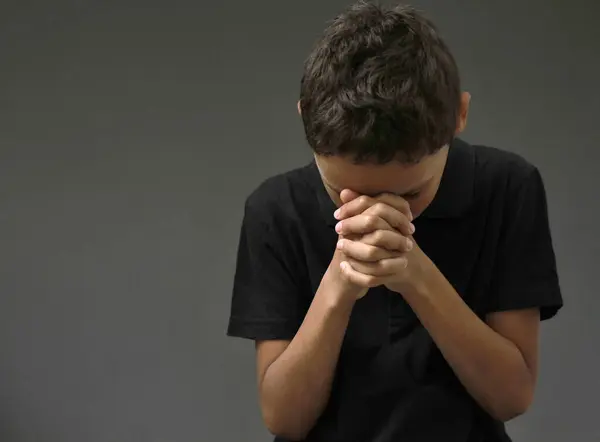 boy praying to God with hands held together with closed eyes on grey background stock photo