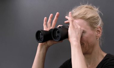 Beyaz arkaplanlı bir spor müsabakasında dürbünle dürbünden bakan bir kadın.