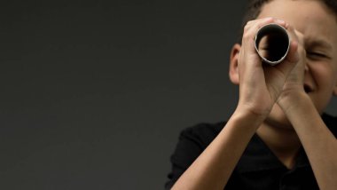 Gri arkaplandaki dürbünlere bakan çocuk insanların resimlerini stokluyor.