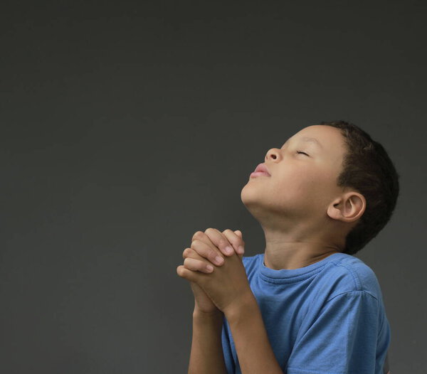 boy praying to God with hands held together with closed eyes with people stock image stock photo