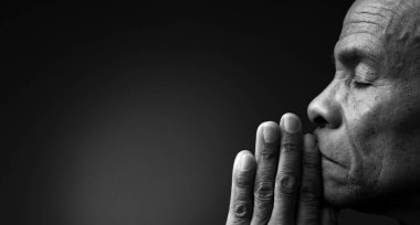 Siyahi adam Tanrı 'ya gri siyah arka planda el ele dua ederken insanların resimlerini stokluyor.