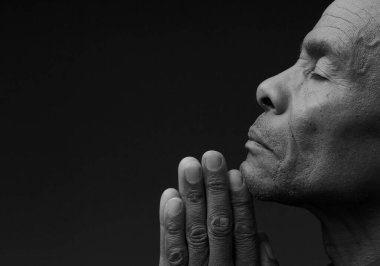 Siyahi adam Tanrı 'ya gri siyah arka planda el ele dua ederken insanların resimlerini stokluyor.