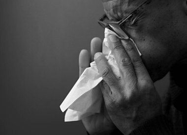 Gri arka planda soğuk algınlığına yakalandıktan sonra burun sümkürme