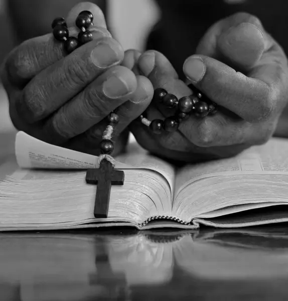 black man people praying to God with hands together on bible with cross