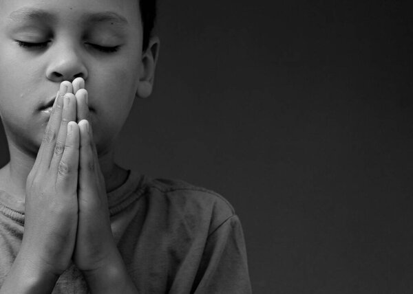 Child boy praying to God with hands together on white background 