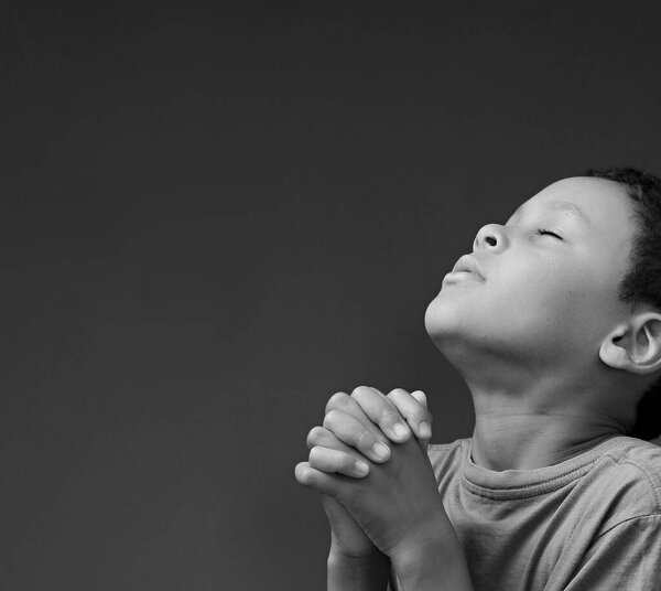 Child boy praying to God with hands together on white background 