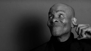 Sağırlık ve işitme kaybından muzdarip olan adam kulaklarını kapatıyor. Siyah ve beyaz parmaklar arka planda. 