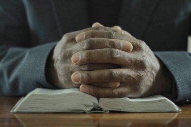 Man praying to god with bible  while sitting at the wooden table, closeup  clipart