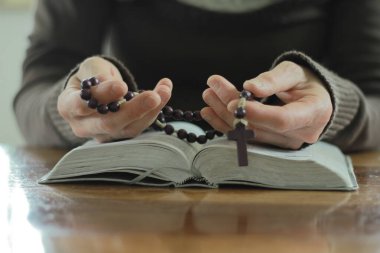 İncil 'le ve haçla Tanrı' ya dua eden kadın ahşap masada otururken, yakın plan. 