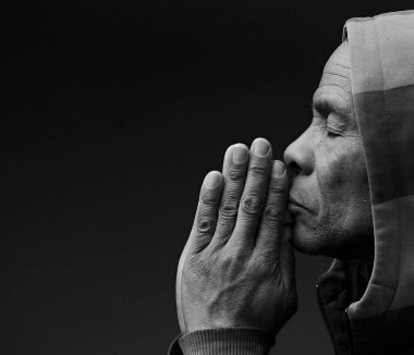 Adam Tanrı 'ya dua ediyor, elleri koyu arkaplanda.