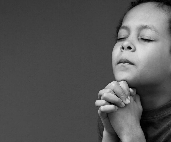 boy praying to God with hands together on black background