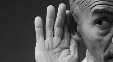 Stüdyoda, elleri kulaklarında, siyah-beyaz kel bir adamın fotoğrafı.