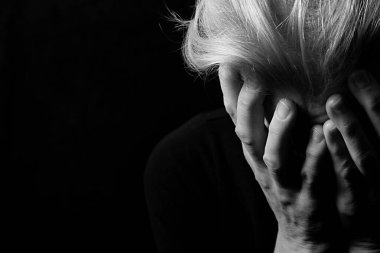 Depresyondan muzdarip bir kadın, elini koyu arka planda tutuyor.