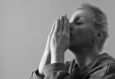 Genç bir kadın gri arka planda dua ediyor. 