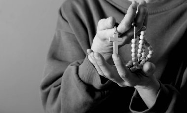 Genç bir kadın ellerinde tespihle dua ediyor. 