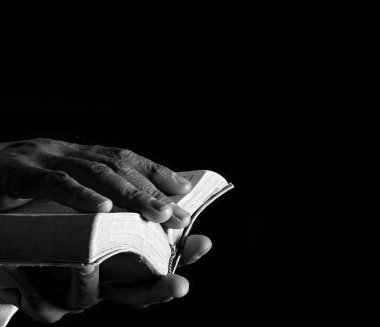 Elinde İncil 'le dua eden bir adam. Siyah arka planda dua eden adam