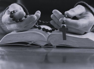 Papaz masada incil ile dua ediyor, haçlı boncukları tutan ellerin kesilmiş görüntüsü. 