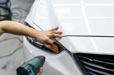 Araba yıkama stüdyosundaki arabanın farına yapıştırılmış koruyucu bir filmin etiketi. Erkek usta sıcak hava tabancası kullanıyor.