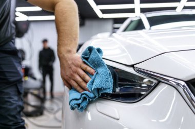 Araba yıkama stüdyosundaki arabanın farına yapıştırılmış koruyucu bir filmin etiketi. Adam bir bez parçasıyla araba siliyor.