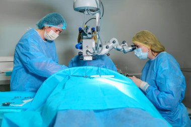 Blepharoplasty plastik cerrahi. Göz çevresindeki bölgenin yenilenmesi ve modifikasyonu. Estetik cerrah ve hemşireler bir kadın hastaya mikroskop kullanarak göz kapağı ameliyatı yapıyorlar.