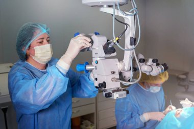 Blepharoplasty plastik cerrahi. Göz çevresindeki bölgenin yenilenmesi ve modifikasyonu. Estetik cerrah ve hemşireler bir kadın hastaya mikroskop kullanarak göz kapağı ameliyatı yapıyorlar.