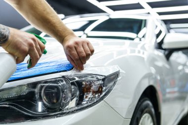 Araba yıkama stüdyosundaki arabanın farına yapıştırılmış koruyucu bir filmin etiketi. Adam sprey tabanca kullanıyor, yakın plan.