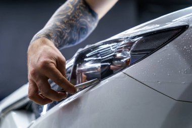 Araba yıkama stüdyosundaki arabanın farına yapıştırılmış koruyucu bir filmin etiketi. Bıçak kullanan bir adam var, yakın plan.