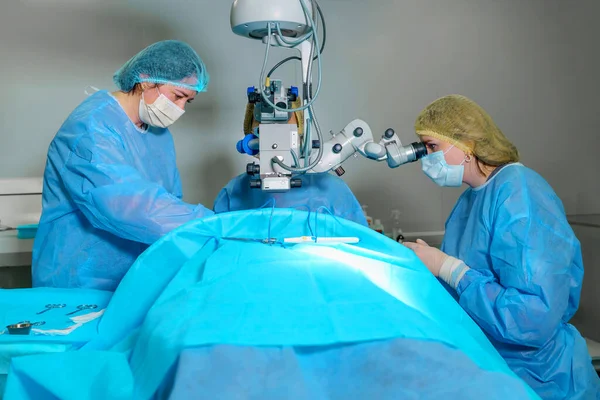 Blepharoplasty plastic surgery. Rejuvenation and modification of the area around the eyes. Plastic surgeon and nurses doing eyelid surgery on a female patient using a microscope