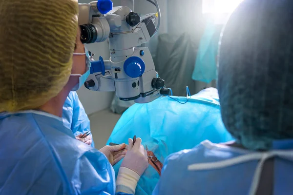 Blepharoplasty plastic surgery. Rejuvenation and modification of the area around the eyes. Plastic surgeon and nurses doing eyelid surgery on a female patient using a microscope