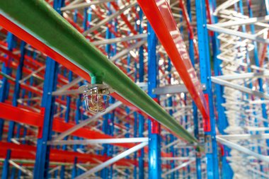 Metal raflı büyük bir depoda yeşil bir boruya yangın fıskiyesi. Yangın söndürücüler, can güvenliği ve yangın koruması için tasarlanmış entegre bir tesisat sisteminin parçasıdır..