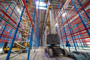 Endüstriyel bir binanın şantiyesindeki hidrolik kaldırma platformu. Uzun metal raf ünitelerini yüklemek için büyük bir depoda makas asansörü kullanılır.