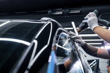Araba yıkama stüdyosundaki arabanın farına yapıştırılmış koruyucu bir filmin etiketi. Erkek usta sıcak hava tabancası kullanıyor.