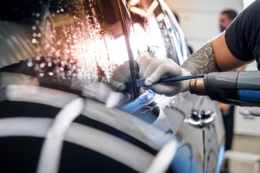 Araba yıkama stüdyosundaki arabanın farına yapıştırılmış koruyucu bir filmin etiketi. Erkek usta sıcak hava tabancası kullanıyor.