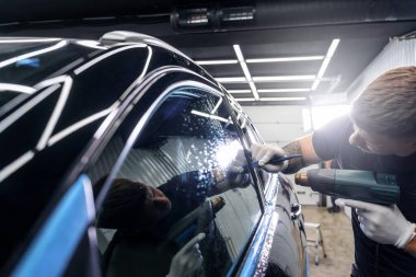 Araba yıkama stüdyosundaki arabanın farına yapıştırılmış koruyucu bir filmin etiketi. Erkek usta sıcak hava tabancası kullanıyor.