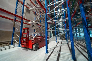 Endüstriyel bir binanın şantiyesindeki hidrolik kaldırma platformu. Uzun metal raf ünitelerini yüklemek için büyük bir depoda makas asansörü kullanılır.