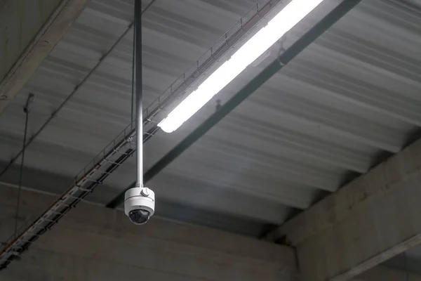 Digital surveillance camera on the ceiling in a warehouse room.