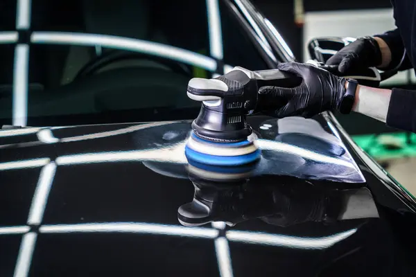 Car detailing and polishing. The hands of a professional car service worker, with an orbital polisher, polishing the hood of a car in a car service center