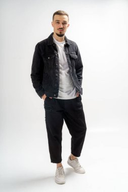 Siyah ceketli, siyah pantolonlu ve gri stüdyo arka planında beyaz tişörtlü yakışıklı bir adam.