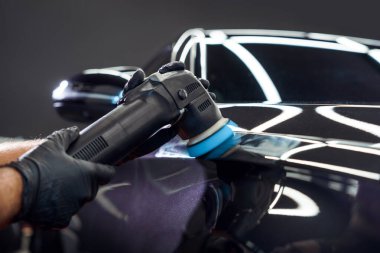 Araba temizliği ve cilalama. Yörünge cilasıyla profesyonel bir araba servisi çalışanının elleri araba servis merkezinde kaputu parlatıyor.