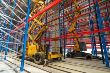 Endüstriyel bir binanın şantiyesindeki hidrolik kaldırma platformu. Uzun metal raf ünitelerini yüklemek için büyük bir depoda makas asansörü kullanılır.