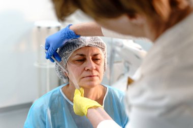 Klinik bir ortamda olgun bir kadın müşteriye estetik estetik ameliyat yaparak cilt tedavisi uygulamasına hazırlanıyor.