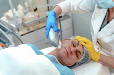 Bir güzellik uzmanı, modern bir güzellik kliniğinde, yetişkin bir kadının yüzünde lazer makinesi kullanır.